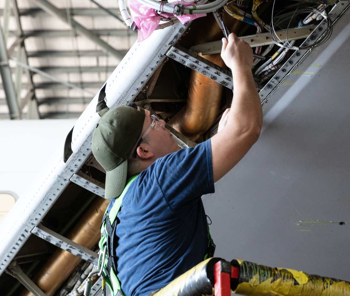 Mechanic with a hat backwards looking up working on a plane